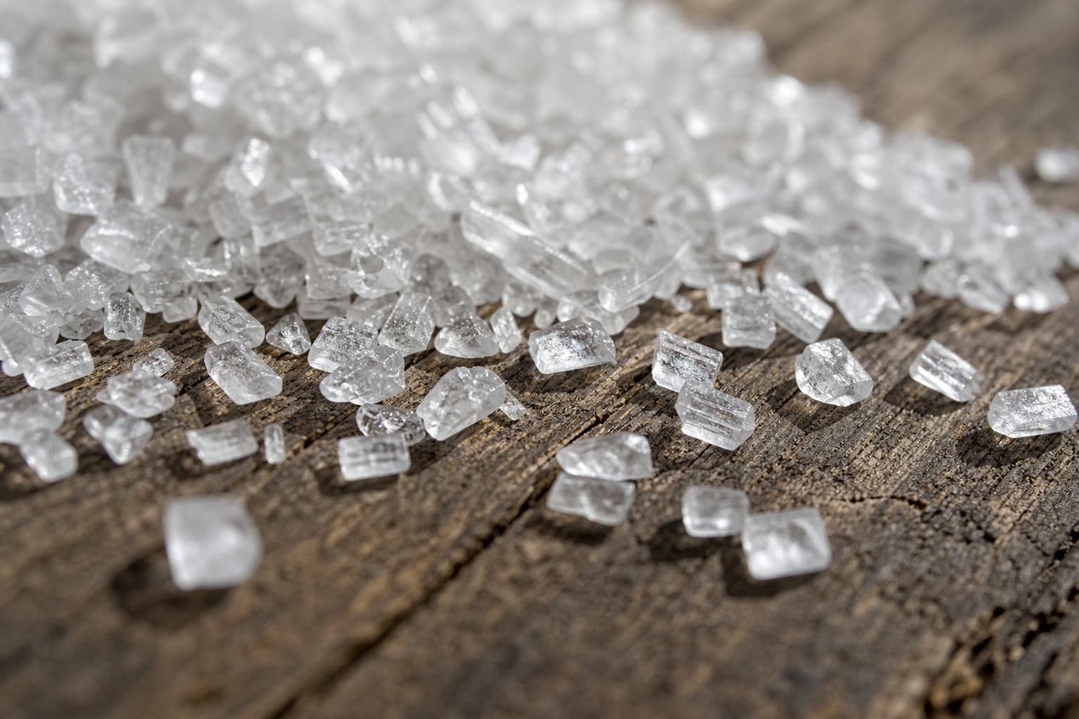 Cristaux translucides de sel d’Epsom dispersés sur une surface en bois rustique, à faible profondeur de champ.